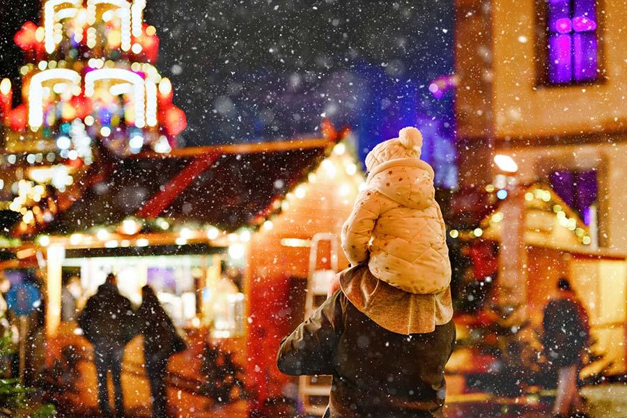 kind op nek kerstmarkt lichtjes sneeuw