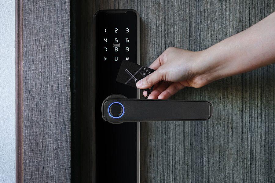 Een zwart digitaal deurslot met deurklink en een hand die het deurslot open maakt met een mechanische sleutel.