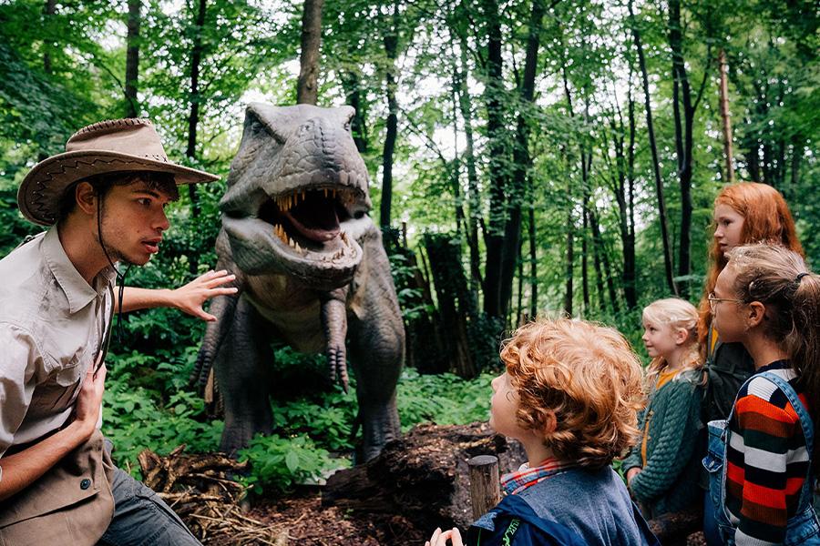 Ranger die aan kinderen vertelt over de levensgrote T-rex op de achtergrond