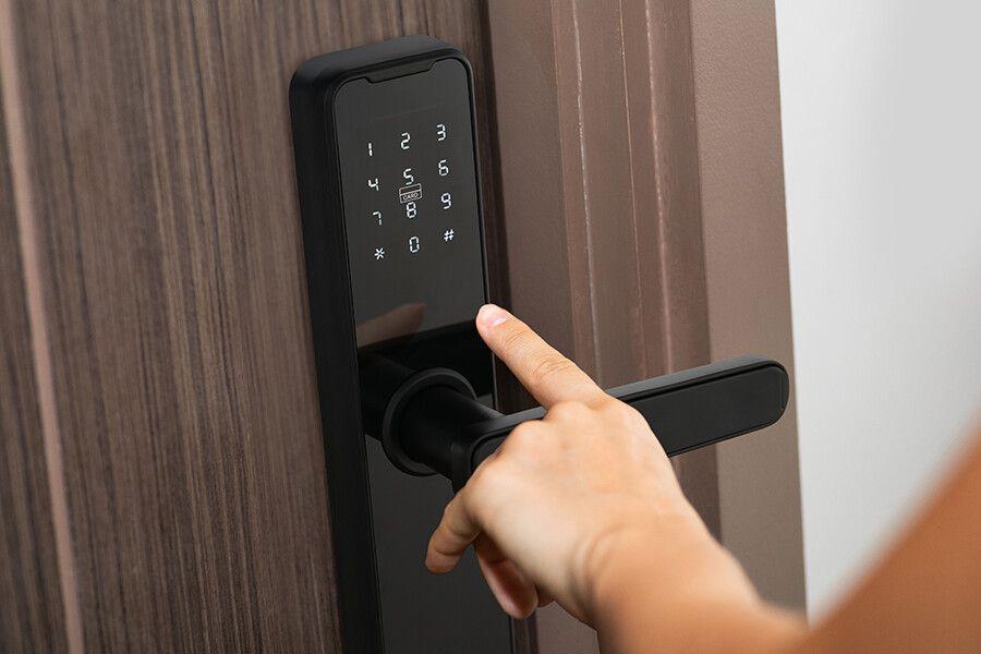 Een zwart digitaal deurslot met deurklink op een bruine deur en een hand die dit slot manueel bedient.