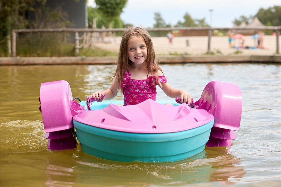 Meisje op een roze waterfiets in het water