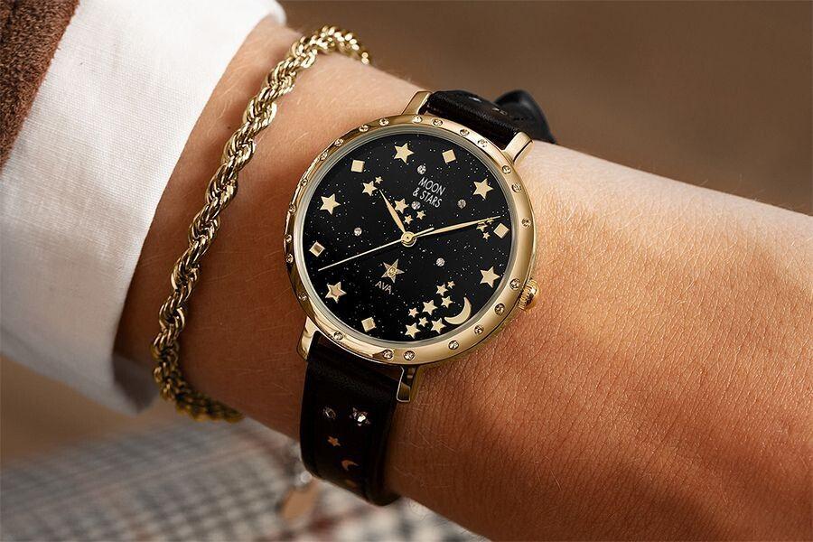 Zwart met goud horloge dat is versierd met manen en sterren achteraanzicht om pols met een goudkleurig armbandje ernaast