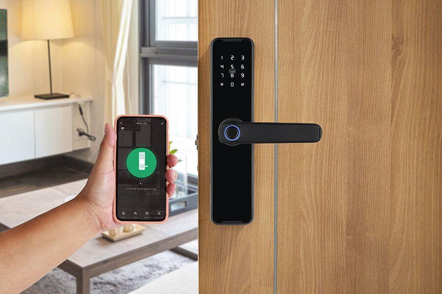 Een zwart digitaal deurslot op een bruine deur en daarnaast een hand met een mobiele telefoon met daarop een app om het slot te bedienen.
